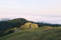 there is a road going down the hill in the distance with clouds rolling over it