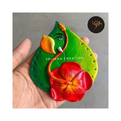 a hand holding a green and red flower brooch