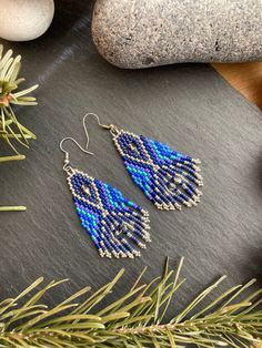 two pairs of beaded earrings sitting on top of a table next to pine needles