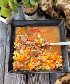 a bowl of soup with carrots, corn and meat in it on a wooden table