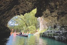 several people in canoes paddling through an underground cave with blue water and trees