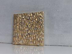 a gold square sculpture sitting on top of a white counter next to a gray wall