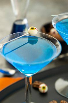 two martini glasses with blue liquid and an eyeball on the rim, sitting on a table