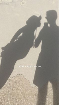 two people standing next to each other in the sand with their shadow on the ground