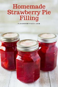 three jars filled with homemade strawberry pie filling on top of a white wooden table and text overlay reads homemade strawberry pie filling