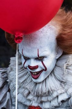 a creepy clown holding a red balloon