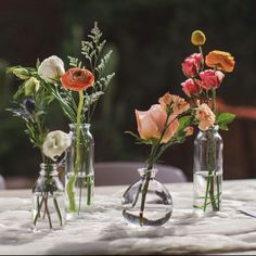 three vases filled with flowers sitting on top of a white tablecloth covered table