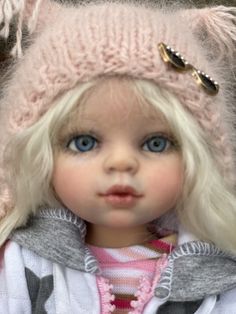 a doll with blonde hair wearing a pink knitted hat and jacket, looking at the camera