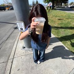 a woman standing on the sidewalk holding up a plastic cup