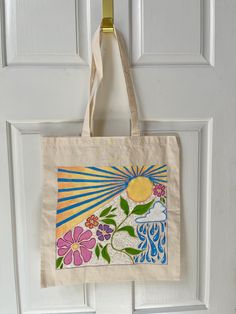 a tote bag hanging on a door handle with flowers and sun in the background