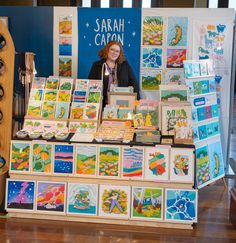 a woman standing behind a table full of cards and magnets on it's sides