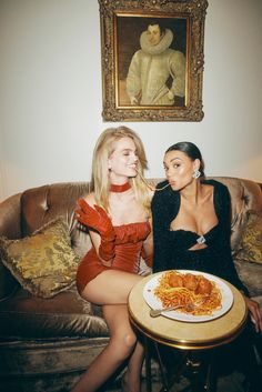 two beautiful women sitting next to each other in front of a table with food on it