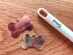 two dog tags are next to a pen on a wooden surface with the word ted written on it