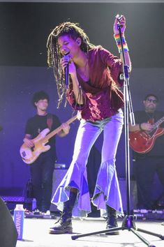 a woman singing into a microphone while holding a guitar in front of other people on stage