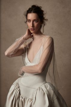 a woman in a white dress poses with her hands on her head and wearing a veil