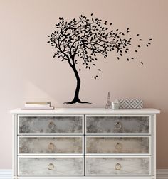 a tree with leaves blowing in the wind on top of a dresser next to a pink wall