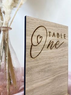 a wooden sign that says table one next to a vase with dried flowers