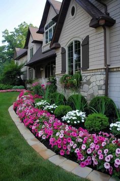 a flower bed in front of a house with pink and white flowers on the side