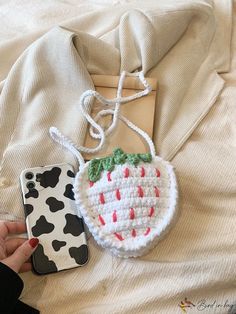 a hand holding a cell phone case next to a crocheted strawberry