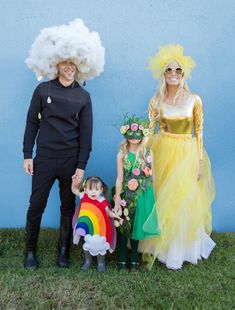 three people dressed up in costumes standing next to each other on the grass with a small child wearing a rainbow costume