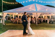 a bride and groom sharing their first dance in front of an outdoor tent at night