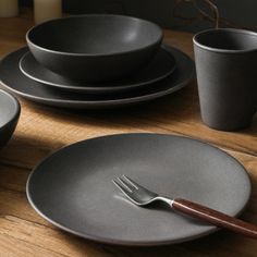 a wooden table topped with black plates and cups