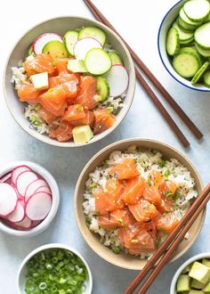 two bowls filled with rice, cucumbers and salmon next to chopsticks