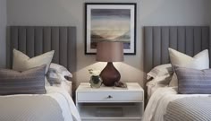 two beds with white and gray bedding in a bedroom next to a lamp on a night stand