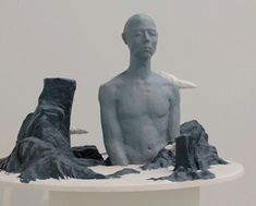 a sculpture of a man sitting on top of a white pedestal next to another statue