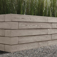 a wooden planter sitting on top of gravel next to tall green plants and grass