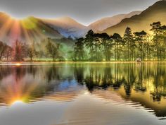 the sun shines brightly over a lake with mountains in the background and trees on both sides