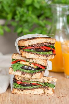 a stack of sandwiches sitting on top of a wooden table next to a glass of orange juice