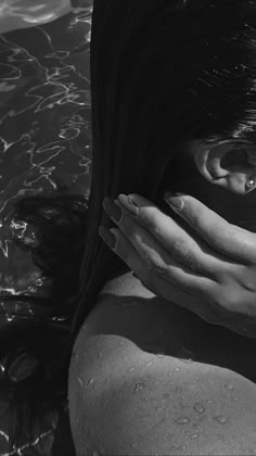 black and white photograph of woman's face with hands over her head in water