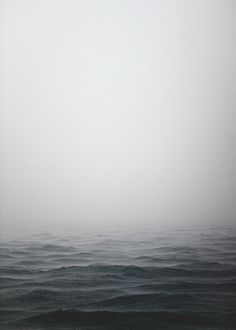 a lone boat floating in the middle of an ocean on a foggy, overcast day