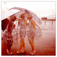 three women dressed in sequins and holding umbrellas pose for a photo together