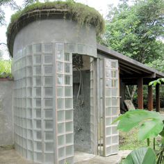 an outdoor shower in the shape of a round building with plants growing out of it