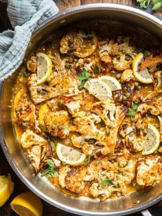 a pan filled with shrimp and lemons on top of a wooden table next to sliced lemons