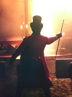 a man with a top hat and cane standing in front of a stage at night