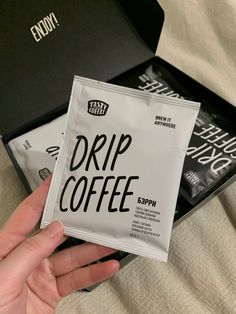 a person holding up a packet of coffee next to a black box with the word drip coffee on it