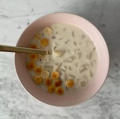 a pink bowl filled with cereal on top of a white counter next to a gold spoon