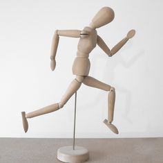 a wooden mannequin running on top of a table in front of a white wall