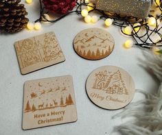 four wooden coasters with merry christmas designs on them next to some pine cones and lights