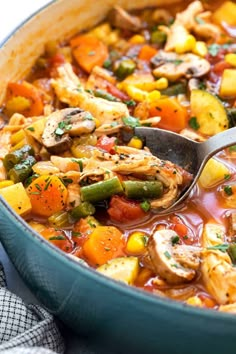 a pot filled with chicken and vegetable stew on top of a blue cloth next to a spoon