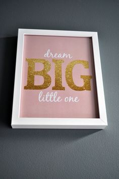 a framed pink and gold print with the words dream big little one in white frame