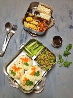 three metal trays filled with food on top of a wooden table next to utensils