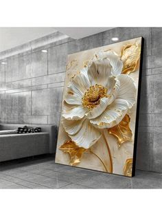 a large white flower with gold leaves on it in front of a gray wall and grey couch