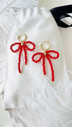 two pairs of red beaded bow earrings sitting on top of a white bag next to feathers