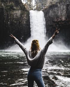 a woman standing in front of a waterfall with her arms spread wide out to the side