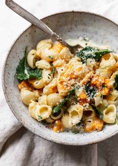 a bowl filled with pasta and spinach covered in parmesan cheese, on top of a white cloth