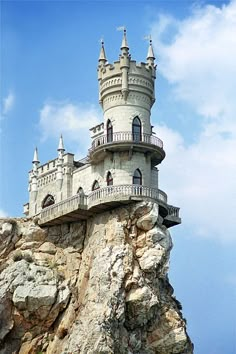 a castle built on the side of a cliff in front of a blue sky with clouds